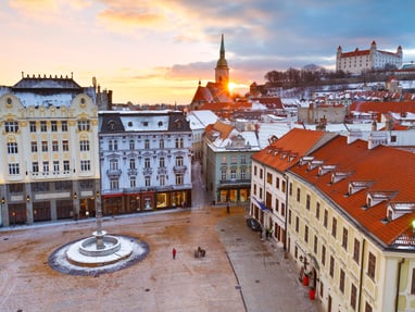 Blick auf schneebedeckten Stadtplatz mit historischen Gebäuden bei Sonnenuntergang.