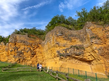 der-steinbruch-carrieres-de-glay-geologisches-unesco-welterb.jpg Besucher betrachten gelbe Steinmauer mit Bäumen oben.