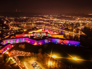 twerenbold_106258.jpg Drohnenansicht einer beleuchteten Festung und Stadt bei Nacht.