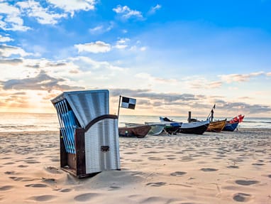 strandkorb-an-der-ostseekueste.jpg Sonnenuntergang am Strand mit Strandkorb und Fischerbooten.