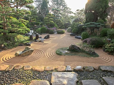 jardin-erik-borja-japanische-gartenkunst-vom-feinsten.jpg Zen-Garten mit Kiesmustern und Steinen, umgeben von Bäumen und Sträuchern.
