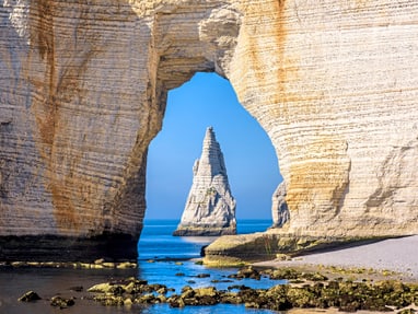 im-fokus-aiguille-d-etretat-die-felsnadel-vor-der-alabasterk.jpg Felsentor am Meer mit freistehendem Felsen im Hintergrund.