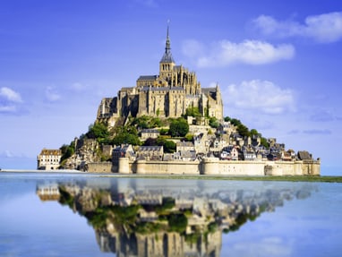 le-mont-saint-michel.jpg Mont Saint-Michel auf felsiger Insel im Meer, blauem Himmel.