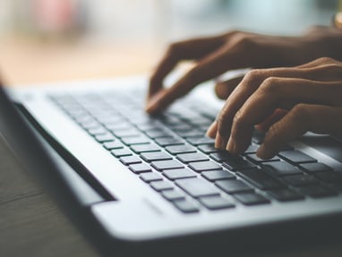 Nahaufnahme von Händen, die auf einer Laptop-Tastatur tippen.