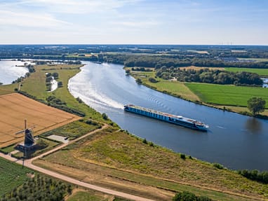excellence-countess.jpg Luftaufnahme eines Flusses mit Schiff und Windmühle in der Landschaft.