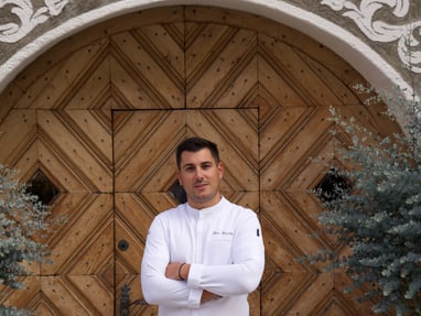 das-excellence-gourmetfestival-4.jpg Mann in weissem Hemd steht vor dekorativer Holztür.