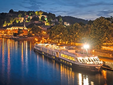 excellence-pearl.jpg Beleuchtetes Flussschiff bei Nacht, umgeben von Hügeln und Bäumen.