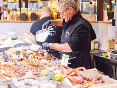 poissonnerie-maison-saiter.jpg Mann hinter einer Fisch- und Meeresfrüchte-Theke auf einem Markt.