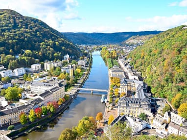 die-weltkulturerbe-stadt-bad-ems-liegt-im-tal-der-lahn.jpg Panoramablick auf Fluss und Stadt zwischen bewaldeten Hügeln.