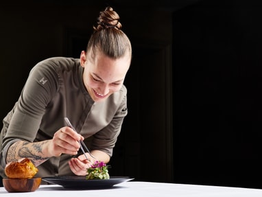 das-excellence-gourmetfestival-10.jpg Person in Kochjacke verziert ein Gericht auf einem Tisch.