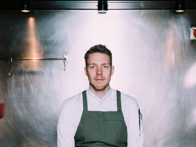 das-excellence-gourmetfestival-10.jpg Mann in grauer Schürze steht in einer Edelstahlküche.