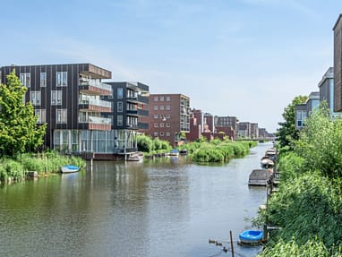 ijburg-moderne-architektur-und-entspanntes-leben-auf-kuenstl.jpg Kanal mit modernen Wohngebäuden und kleinen Booten entlang des Ufers.