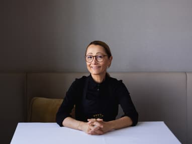 Frau mit Brille und dunklem Oberteil sitzt an einem Tisch.
