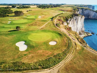 club-golf-detretat.jpg Landschaft mit Küstenklippen, grünen Feldern und Golfplätzen neben dem Meer.