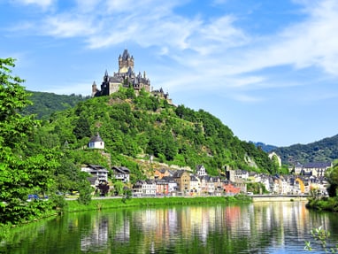 die-reichsburg-bei-cochem.jpg Burg auf einem Hügel über einer Stadt am Fluss.