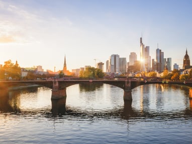 die-schillernde-skyline-von-frankfurt-hinter-der-ignatz-bubi.jpg Stadtansicht mit Fluss und Brücke bei Sonnenuntergang.