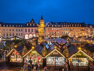 weihnachtsmarkt-in-trier.jpg Abendlicher Weihnachtsmarkt mit Lichtern und Ständen in einer historischen Stadt.
