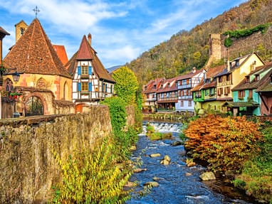 Eine malerische Altstadt mit Fachwerkhäusern, Fluss und herbstlichen Bäumen.