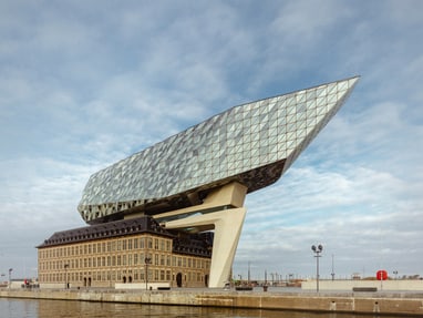 das-antwerpener-havenhuis-thront-wie-ein-riesiger-diamant-ue.jpg Modernes Gebäude mit glasüberdachtem Dach über historischem Backsteingebäude am Wasser.