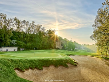 mainzer-golfclub.jpg Sonnenaufgang über einem Golfplatz mit Bunker und Bäumen.