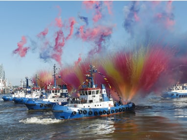schlepperballett-am-hamburger-hafengeburtstag.jpg Mehrere Schlepperboote sprühen bunte Wasserfontänen im Hafen.