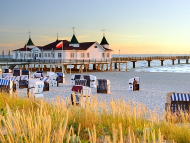 historische-seebaeder-am-40-kilometer-langen-sandstrand-auf.jpg Strandkörbe am Sandstrand vor Seebrücke in der Abenddämmerung.