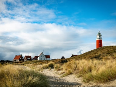 westfriesland-die-wattenmeer-insel-texel.jpg Roter Leuchtturm auf Düne mit Häusern im Hintergrund.