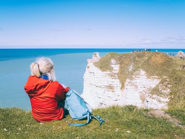 seebrise-atmen-natur-entdecken-klippenwanderung-an-der-felse.jpg Person in roter Jacke sitzt auf einer Klippe mit Blick auf das Meer.