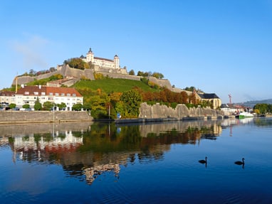 Festung auf Hügel am Flussufer mit Enten im Wasser.
