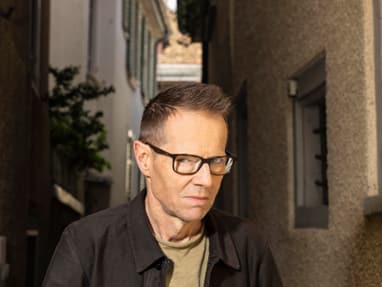baenz-friedli.jpg Mann mit Brille geht durch enge Gasse mit hohen Gebäuden.