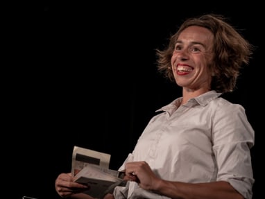 claire-alleene.jpg Person in einem weissen Hemd hält ein Buch und lächelt.