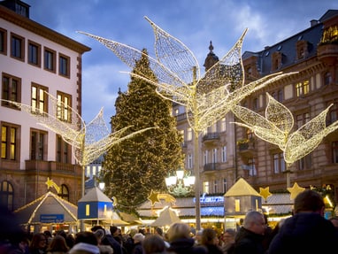 Weihnachtsmarkt mit Lichtdekorationen und grossen Gebäuden im Hintergrund.