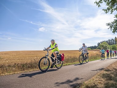 velofahren-in-der-idyllischen-normandie.jpg Gruppe von Radfahrern auf ländlichem Weg bei sonnigem Wetter.