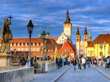 wuerzburg.jpg Menschen auf mittelalterlicher Brücke mit Kirche im Hintergrund.