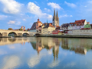 regensburg.jpg Flussblick auf mittelalterliche Stadt mit Brücke und Kirchtürmen.