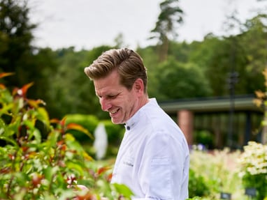 Person in weissem Hemd steht im Garten umgeben von Pflanzen.