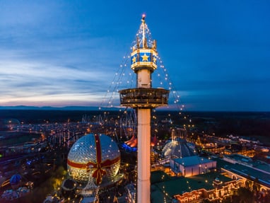 per-schiff-zum-europa-park-6.jpg Abendansicht eines beleuchteten Vergnügungsparks mit Turm und Glaskuppel.