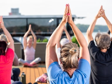yoga-auf-dem-sonnendeck.jpg Gruppe von Menschen macht Yoga im Freien mit erhobenen Armen.