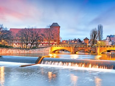 nuernberg.jpg Fluss in Nürnberg mit beleuchtetem Brückenbogen und Gebäuden im Hintergrund.