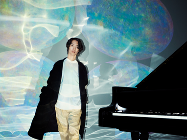 klavierlegende-hayato-sumino.png Mensch neben einem Flügel vor bunter Lichtprojektion.