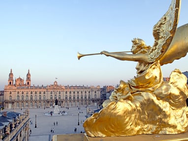 nancy-place-stanislas.jpg Goldene Statue mit Trompete auf Balkon mit Blick über grossen Platz und historische Gebäude.