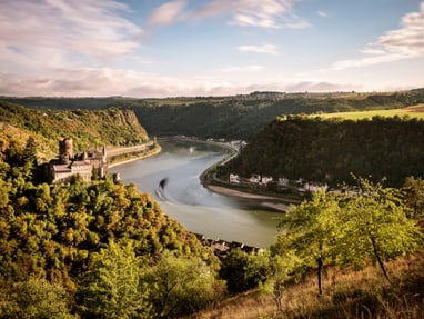 oberes-mittelrheintal-ein-romantisches-unesco-welterbe.jpg Burgruine am Fluss mit bewaldeten Hügeln im Hintergrund.