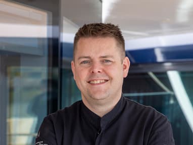 klingt-gut-schmeckt-gut-die-donau-mit-sternekoch-stefan-heil.jpg Mann in dunkler Uniform steht mit verschränkten Armen in einem modernen Raum.