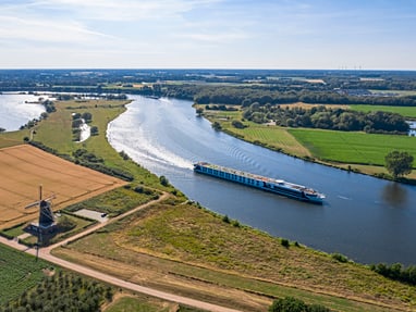 excellence-countess.jpg Luftaufnahme eines Flusses mit Schiff und Windmühle in der Landschaft.