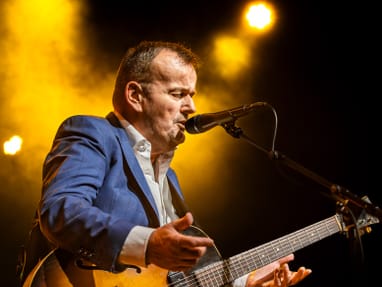 Mann in blauem Anzug spielt Gitarre auf der Bühne.