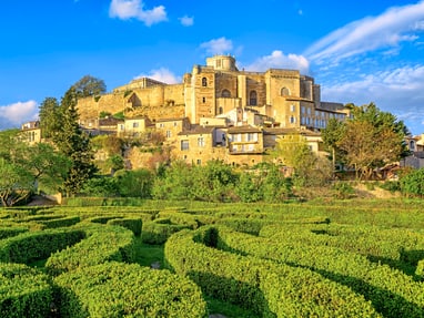 dorf-grignan.jpg Historische Burg auf einem Hügel mit Labyrinth aus Hecken im Vordergrund.