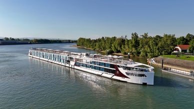 Flusskreuzfahrtschiff fährt auf einem Fluss, mit Bäumen am Ufer.