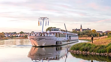 excellence-coral.jpg Flusskreuzfahrtschiff auf ruhigem Wasser nahe Ufer und Dorf.