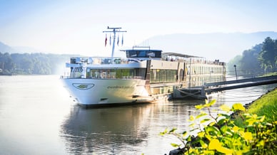 Flusskreuzfahrtschiff auf ruhigem Fluss bei sonnigem Wetter.