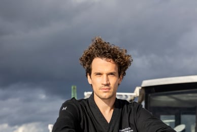das-excellence-gourmetfestival-4.jpg Mann in schwarzer Kleidung sitzt auf einem Boot mit bewölktem Himmel im Hintergrund.